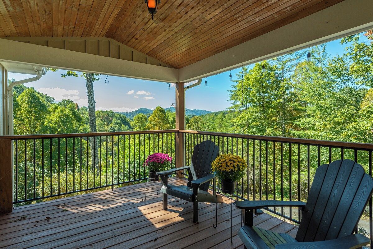 A wooden deck with a railing, two Adirondack chairs, and potted plants.
