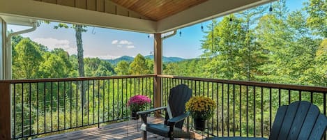 A wooden deck with a railing, two Adirondack chairs, and potted plants.
