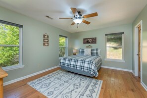 A bedroom with a bed, a ceiling fan, a rug, and two windows.