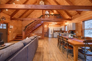 Ein Holzblockhaus-Interieur mit Treppe, einer Küche und einem Wohnbereich mit Sofa und Esstisch.