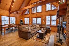 A cozy cabin interior with a wooden dining table, a sofa, and a fireplace. - White Tail Ridge: WALK to Old Man’s Cave + Hot Tub (Logan)
