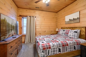 A wooden cabin room with a bed, a dresser, a television, and a window with curtains. - White Tail Ridge: WALK to Old Man’s Cave + Hot Tub (Logan)