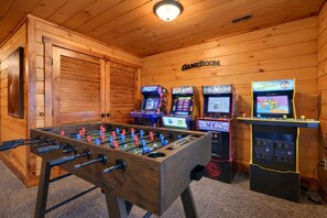 Een kamer met houten vloer, een tafelvoetbaltafel, drie gokautomaten en een gesloten luik.