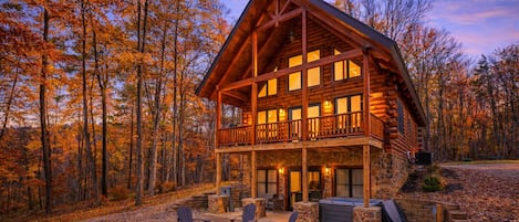 A log cabin with a balcony, a fire pit, and outdoor seating.
