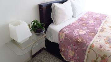 Una camera da letto ordinata con un letto, cuscini, un comodino con una lampada e una pianta in vaso, e una mensola in vetro.