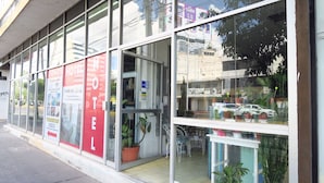 A hotel with large windows, a visible entrance, and potted plants inside. - Hotel Llanito (Aguascalientes)