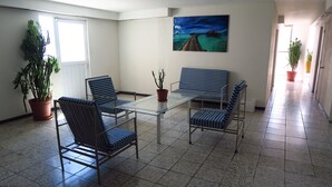 A spacious room with a glass table and striped chairs, a large window, and a painting of a pier. - Hotel Llanito (Aguascalientes)