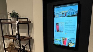 A home interior with a digital display on a wall, a wooden shelving unit with decorative items, and a small potted plant. - Modern 4b 2bth Roseville Retreat with a spa Near Thunder Valley + The Grounds (Roseville)