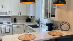 A modern kitchen with white cabinets, a granite countertop, two black bar stools, and pendant lights with orange shades. - Modern 4b 2bth Roseville Retreat with a spa Near Thunder Valley + The Grounds (Roseville)