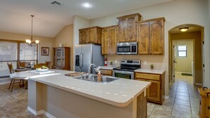 Una cocina con armarios de madera, un refrigerador de acero inoxidable, un microondas y una isla grande con un lavamanos.