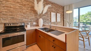 A modern kitchen with a stone backsplash, stainless steel appliances, wooden cabinets, and a large window providing a view of the outdoors. - Rooftop w/ Views: Modern Little Italy Townhome (San Diego)