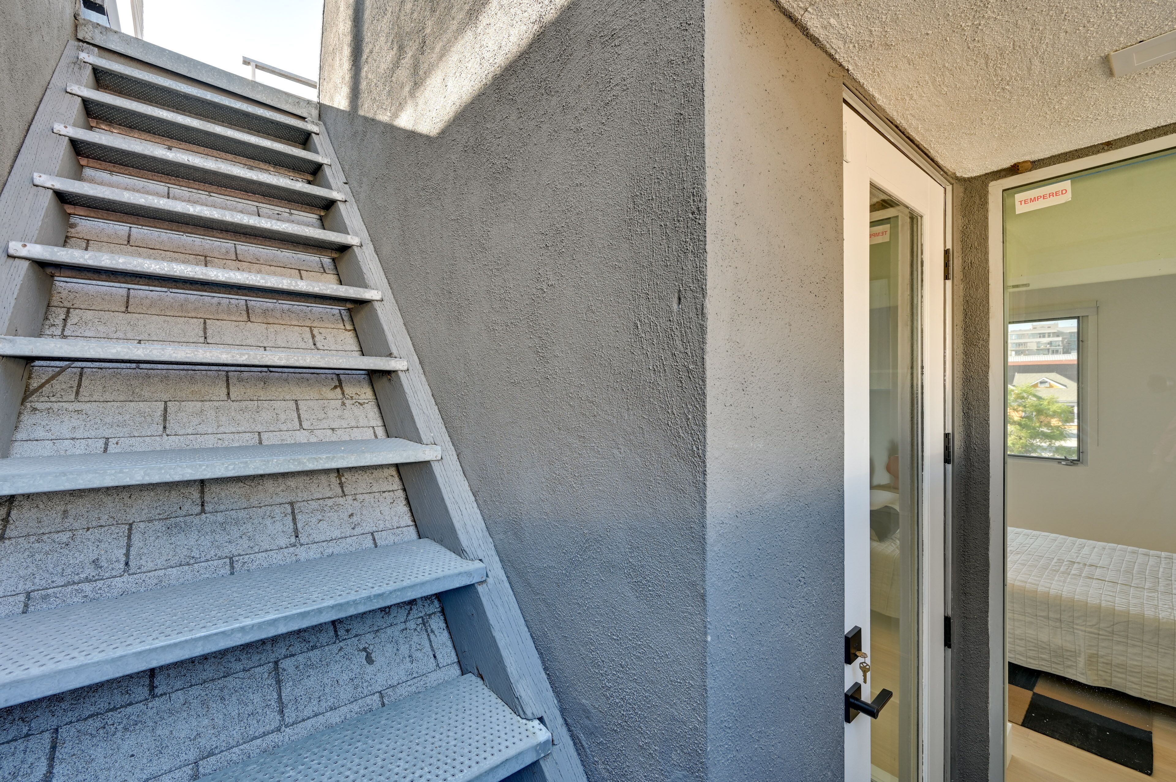 A staircase leading to a room with a bed, a door with a 'Tempered' sign, and a window.