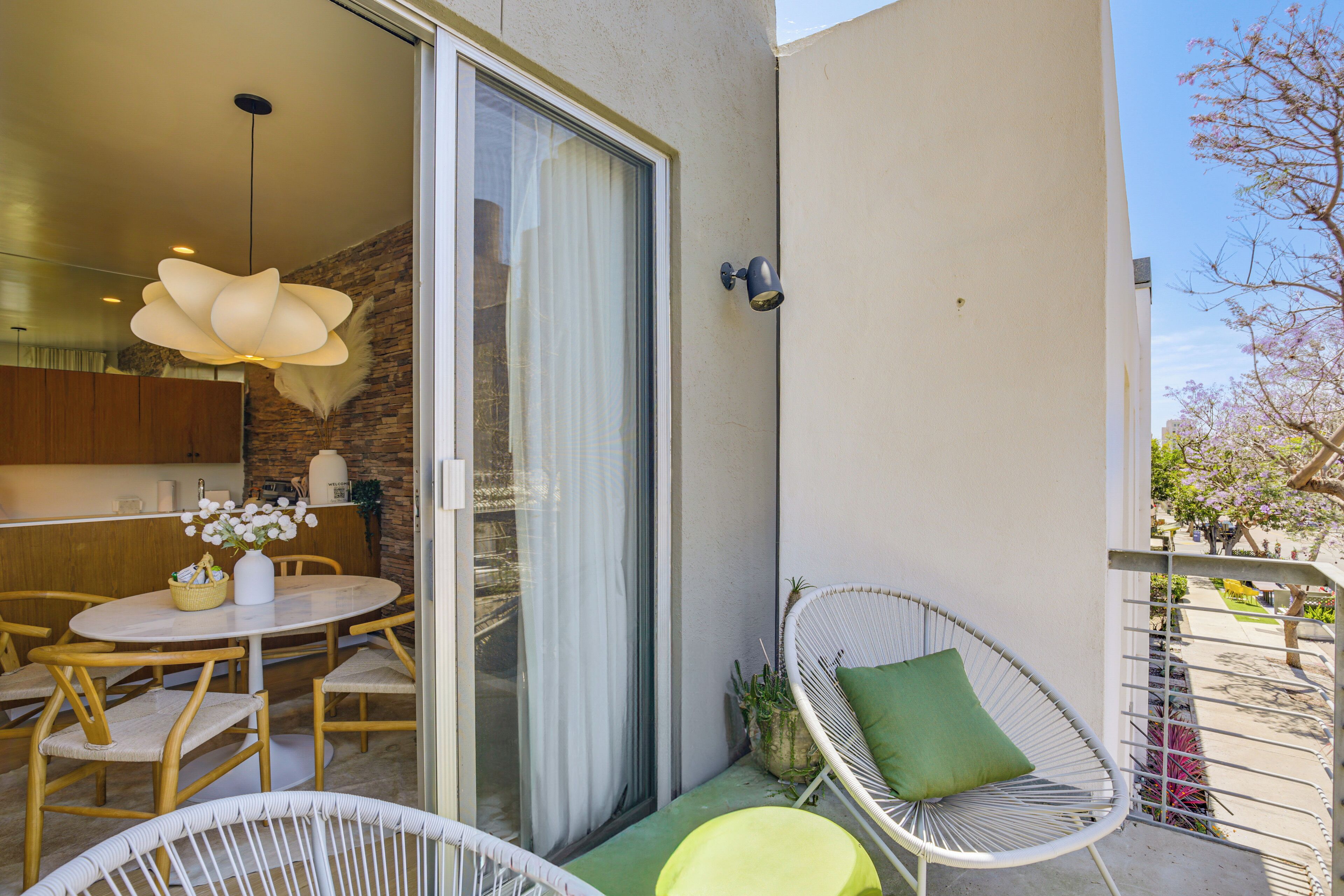 Un balcon avec un coin repas, une chaise en osier, une plante en pot et une vue sur la rue.
