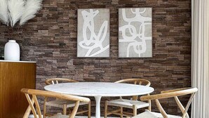 A dining area with a round table, wooden chairs, a white rug, a stone wall, and abstract art pieces. - Rooftop w/ Views: Modern Little Italy Townhome (San Diego)