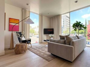 Uma sala de estar moderna com um sofá, uma TV, um abajur e uma janela ampla com vista para a cidade.