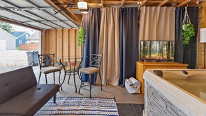 A garage converted into a cozy living space with a sofa, chairs, a hot tub, and curtains.