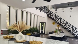 Un intérieur moderne avec un îlot central, un escalier noir et une vue sur l’extérieur.