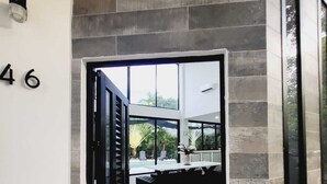 Une entrée moderne avec une façade en pierre, une porte noire et une vue sur un espace piscine.