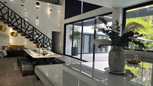 Un salon moderne avec une grande table en verre, un escalier noir et une vue sur l’extérieur.