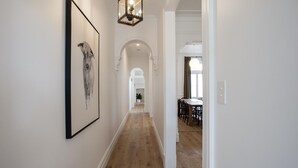 Un couloir doté d’un plancher en bois, de murs blancs et d’une œuvre d’art encadrée. On aperçoit une salle à manger avec une table et des chaises à travers une porte ouverte.