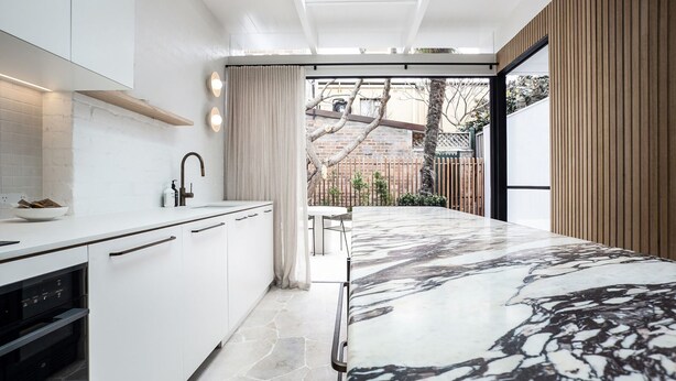 Une cuisine moderne avec des meubles blancs, un plan de travail en marbre et une vue sur le jardin arrière.
