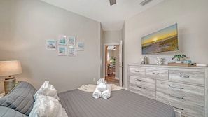 Un dormitorio con cama, cómoda, televisor y cuadros en la pared.