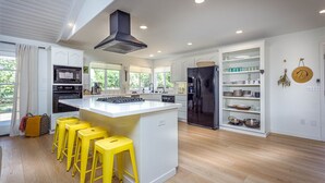 Una cocina moderna con una isla central, taburetes amarillos, un refrigerador negro y muebles de cocina blancos.