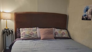 Un lit avec une tête de lit marron, un oreiller à motifs et une couvre-lit unie.