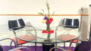 Une salle de conférence avec une table en verre, quatre chaises, un vase de fleurs et deux tableaux abstraits accrochés au mur.