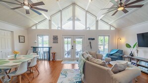 A spacious living area with a high ceiling, ceiling fans, a dining area with a table and chairs, and a seating area with a sofa and ottoman.
