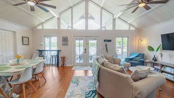 Un vaste espace de vie doté d’un haut plafond et de ventilateurs de plafond, un coin repas avec une table et des chaises, et un coin salon avec un canapé et un pouf.