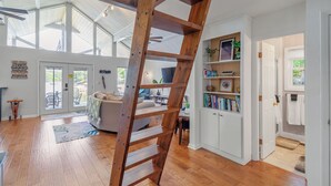 A spacious living area with a wooden ladder, a sofa, a bookshelf, and a view of the outdoors.