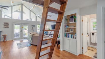 Un espace de vie spacieux avec une échelle en bois, un canapé, une bibliothèque et une vue sur l’extérieur.