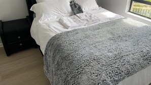 A neatly made bed with white linens and a gray blanket, a black nightstand with drawers, and a window with a view of greenery. - On a golf estate with Mountain views.
4km from the Beach (Cape Town)