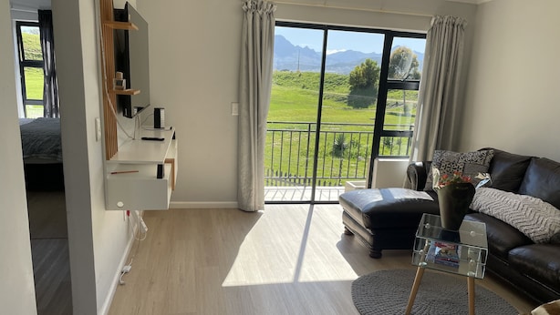 A modern living room with a large sliding glass door leading to a balcony, a leather sofa, a glass coffee table, and a small side table. - On a golf estate with Mountain views.
4km from the Beach (Cape Town)