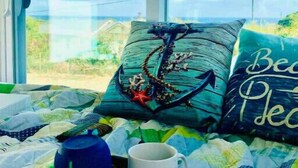 Un lit avec une courtepointe, un oreiller orné d’un motif d’ancre, une tasse et un objet en forme de croix.