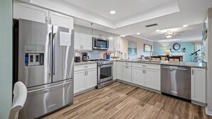 A modern kitchen with stainless steel appliances, white cabinetry, and a herringbone wood floor.