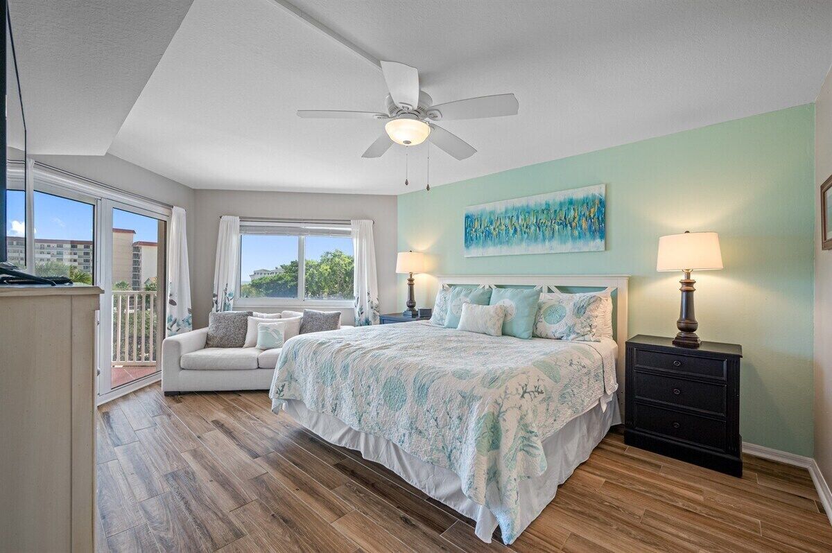 A bedroom with a bed, a nightstand, a ceiling fan, a window, and a painting on the wall.