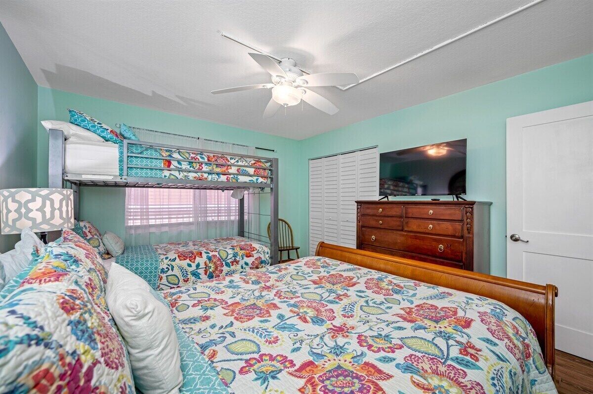 Un dormitorio con una cama litera, una cama individual, un ventilador de techo, un aparador y un televisor.