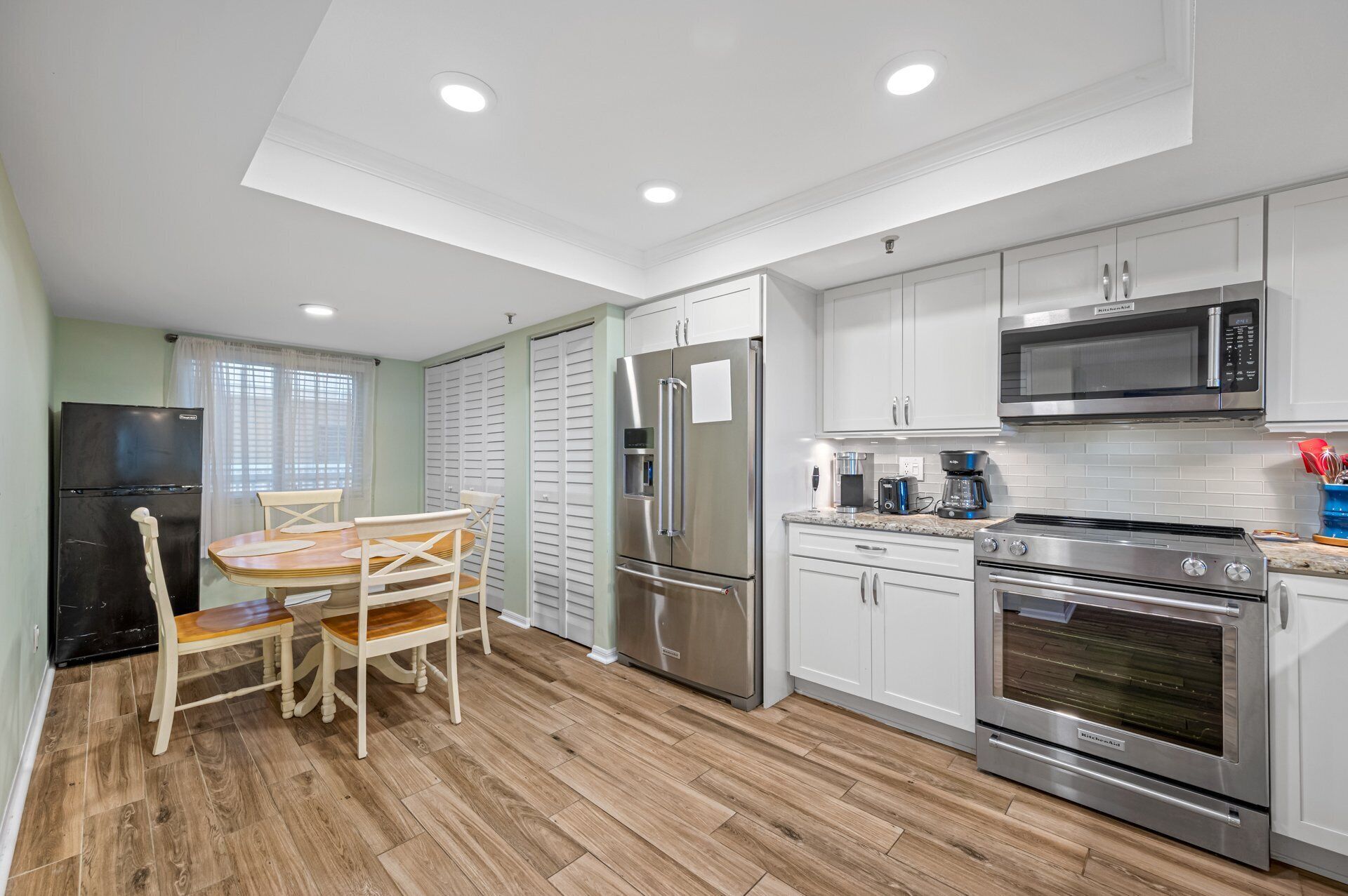 A modern kitchen with white cabinets, stainless steel appliances, and a wooden dining table with chairs.
