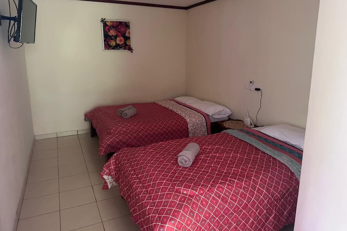 A small, clean room with two beds, a wall-mounted TV, and a power outlet.
