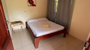 A bedroom with a wooden bed, a small bedside table, a wall-mounted air conditioner, and a window with curtains. - Riverside Lodge (Las Horquetas)