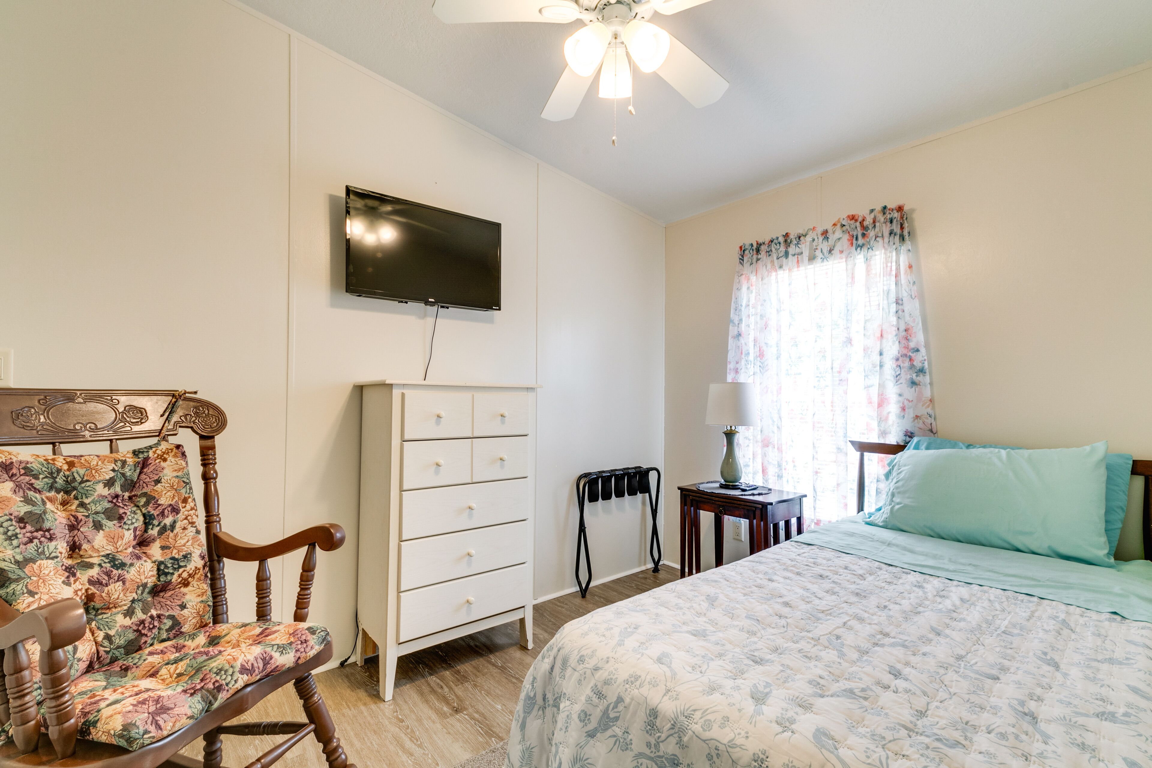 A bedroom with a bed, a dresser, a chair, a television, and a ceiling fan.