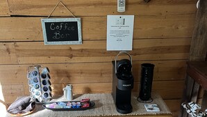 Una mesa de madera con una cafetera, un hervidor y una bandeja con tazas de café. Hay un reloj en la pared y un letrero que dice "Coffee Bar".