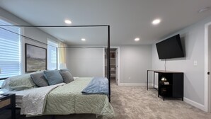 Un dormitorio con cama con dosel, un televisor de pantalla plana en la pared y un vestidor.