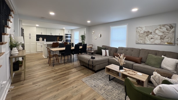 Una sala moderna con un sofá seccional, un comedor con mesa de madera y una cocina con armarios blancos.