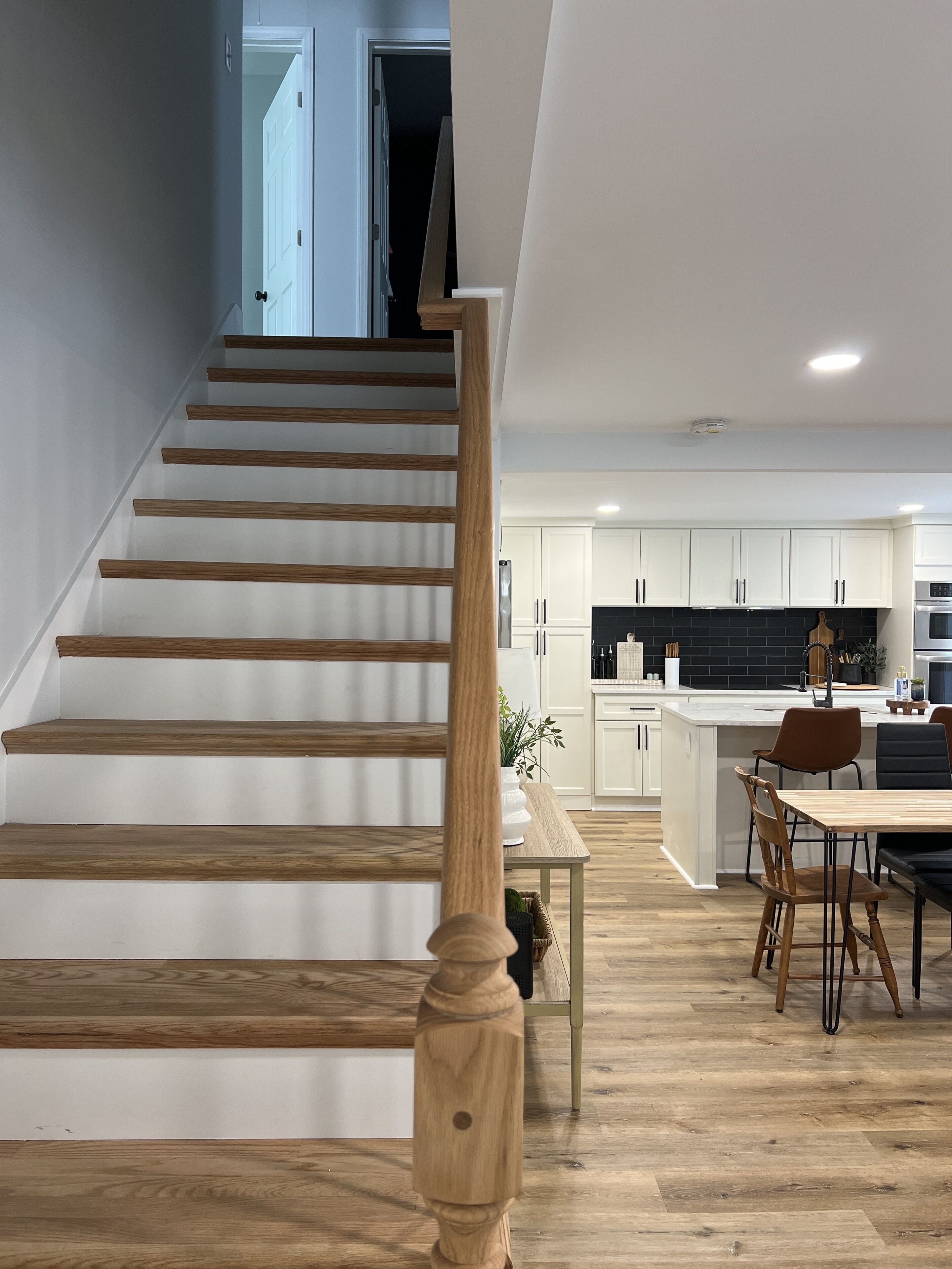 Une cuisine moderne avec des meubles blancs, un îlot central et un coin repas doté de chaises en bois.
