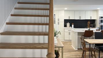 Une cuisine moderne avec des meubles blancs, un îlot central et un coin repas doté de chaises en bois.