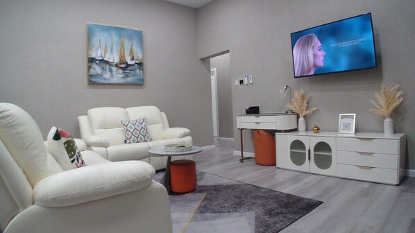 A modern living room with a white sofa, a coffee table, a TV mounted on the wall, and a decorative painting.