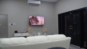 A modern living room with a white sofa, a flat-screen TV mounted on the wall, a small side table with decorative items, and a black door. - 2BR Modern Golden Pear Villa, Pool, Wi-Fi, Kitchen, Views – Family/Group Ready (Saint David)